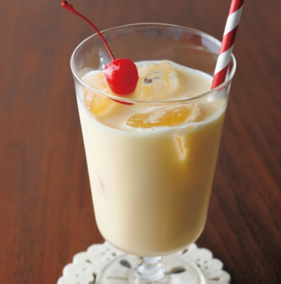 A tall stemmed glass of creamy, pale-yellow mirukusēki over ice, topped with a maraschino cherry and a red-and-white striped straw.