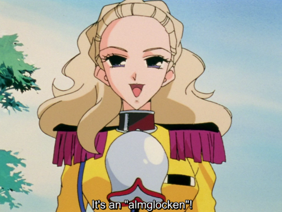 Nanami, wearing a yellow jacket with fringed epaulettes, smiles brightly with a large silver cowbell hanging from a collar around her neck. The subtitle reads "It's an "almglocken"!"