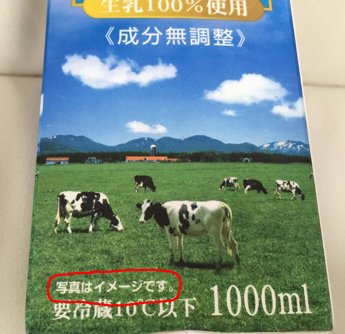 Photo of a Japanese milk carton showing Holstein cows grazing in a green field beneath mountains and a blue sky. Text on the carton includes “生乳100%使用”, “《成分無調整》” and “1000ml”, and the disclaimer “写真はイメージです。” (the photo is an image) is circled in red.