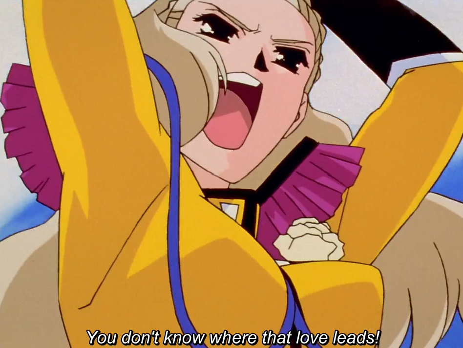 Nanami, in her yellow duelling outfit, shouts with one arm raised. The subtitle reads “You don’t know where that love leads!”