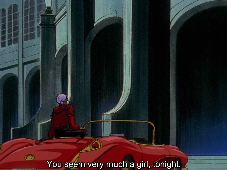 At night, Akio, seen from behind, sits on the back of his red convertible in front of a large arched building. The subtitle reads “You seem very much a girl, tonight.”